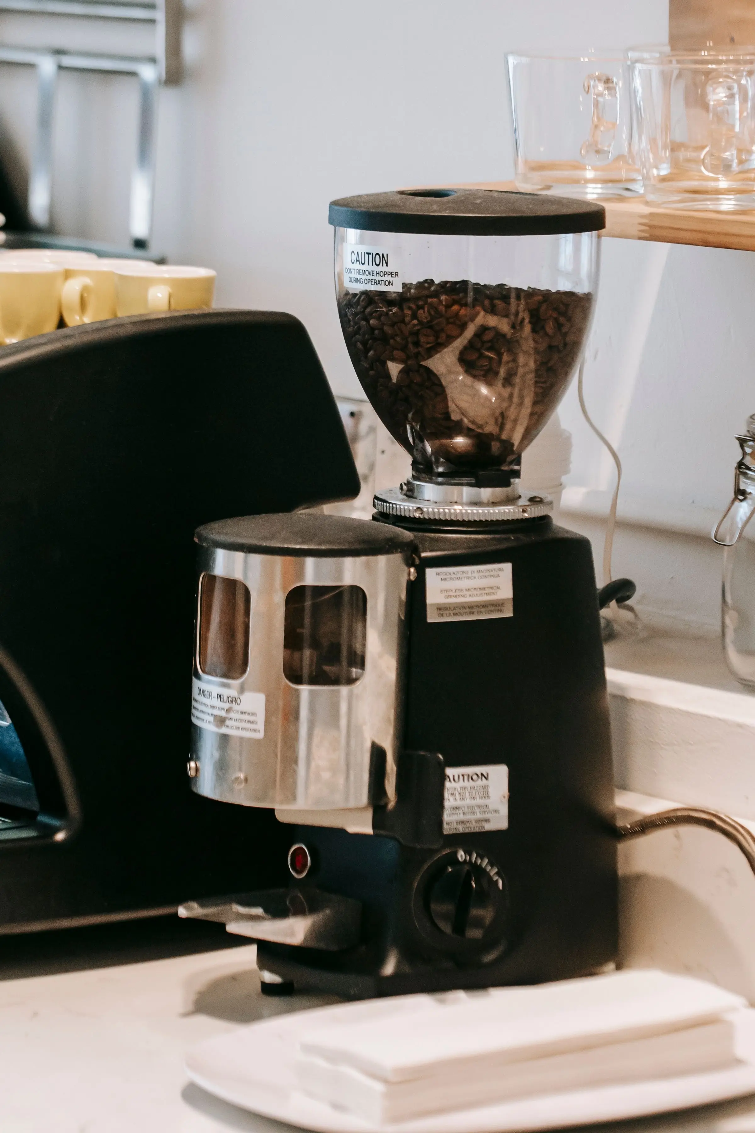 A black coffee grinder with a clear hopper of roasted beans and a dial on the front, on a pale kitchen counter.