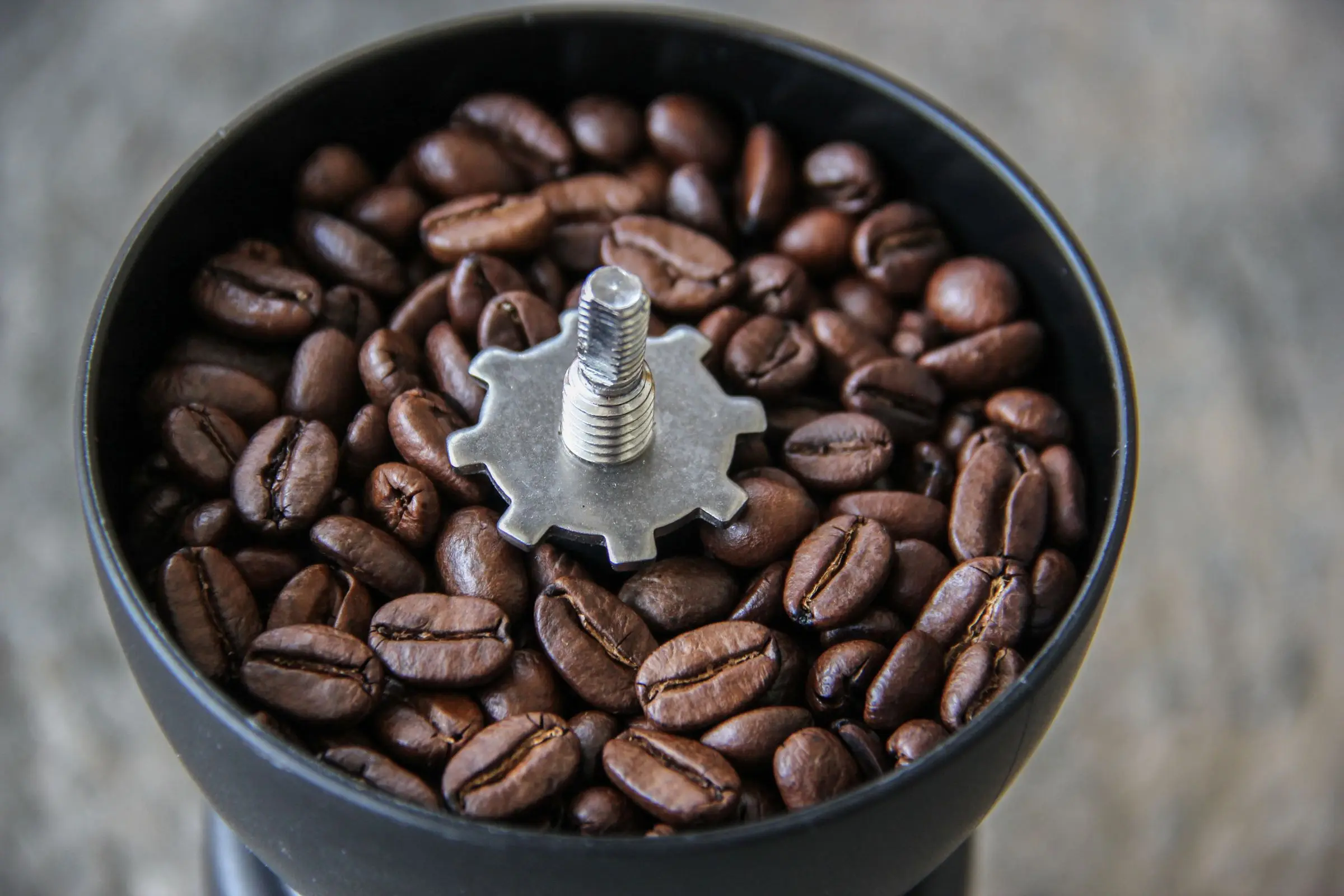 Coffee beans around the burr shaft of a grinder, seen from above.